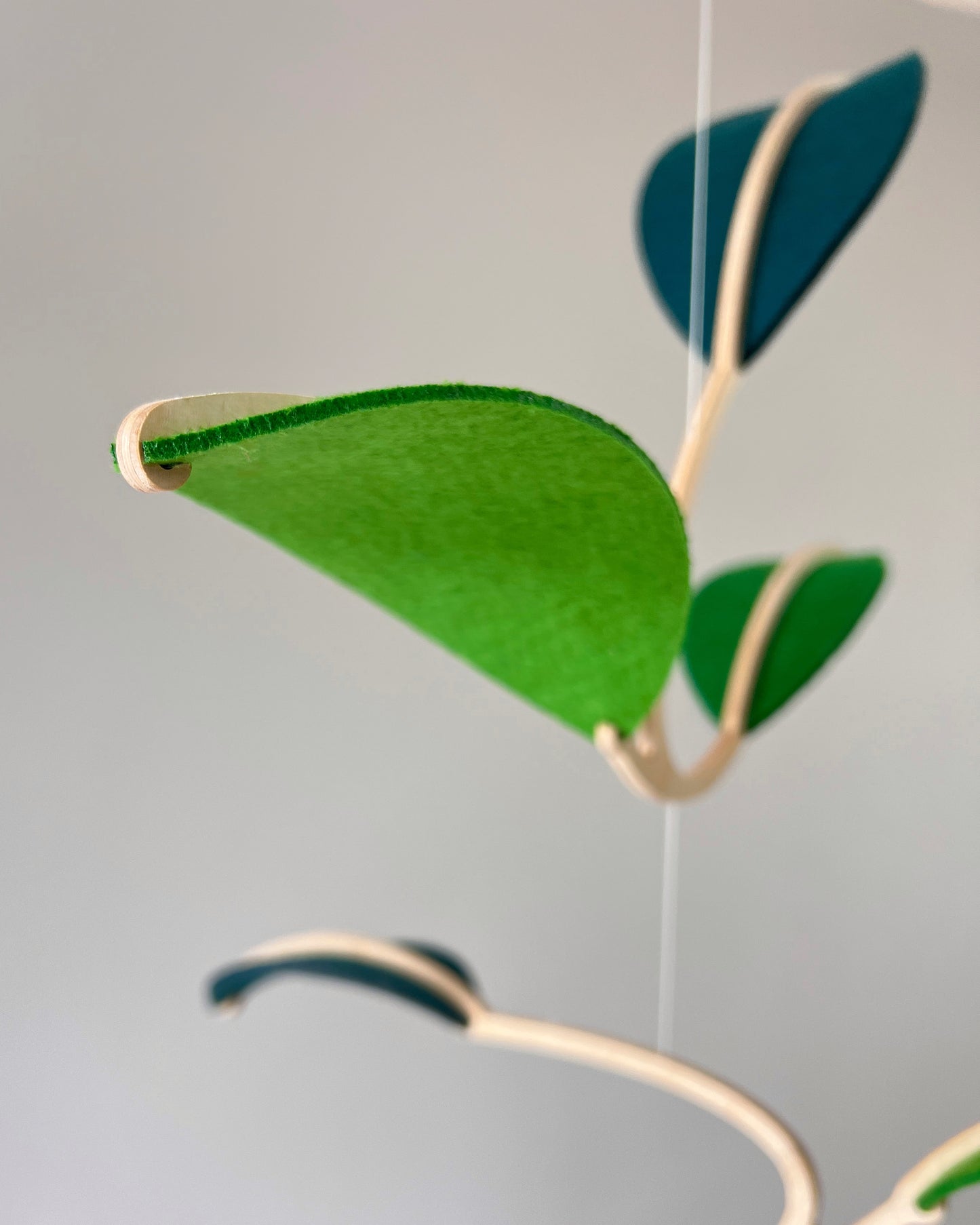 Felt Leaf Mobile 

   Elevate your space with this versatile Midcentury Modern Mobile, designed for both nurseries and adult living areas. Crafted from natural wood with deep teal and green shades of soft felt, this handmade nursery mobile embodies a minimalist and Scandinavian aesthetic. Its unique geometric design creates a stunning hanging sculpture that fits seamlessly into nursery decor and neutral relaxing spaces. 