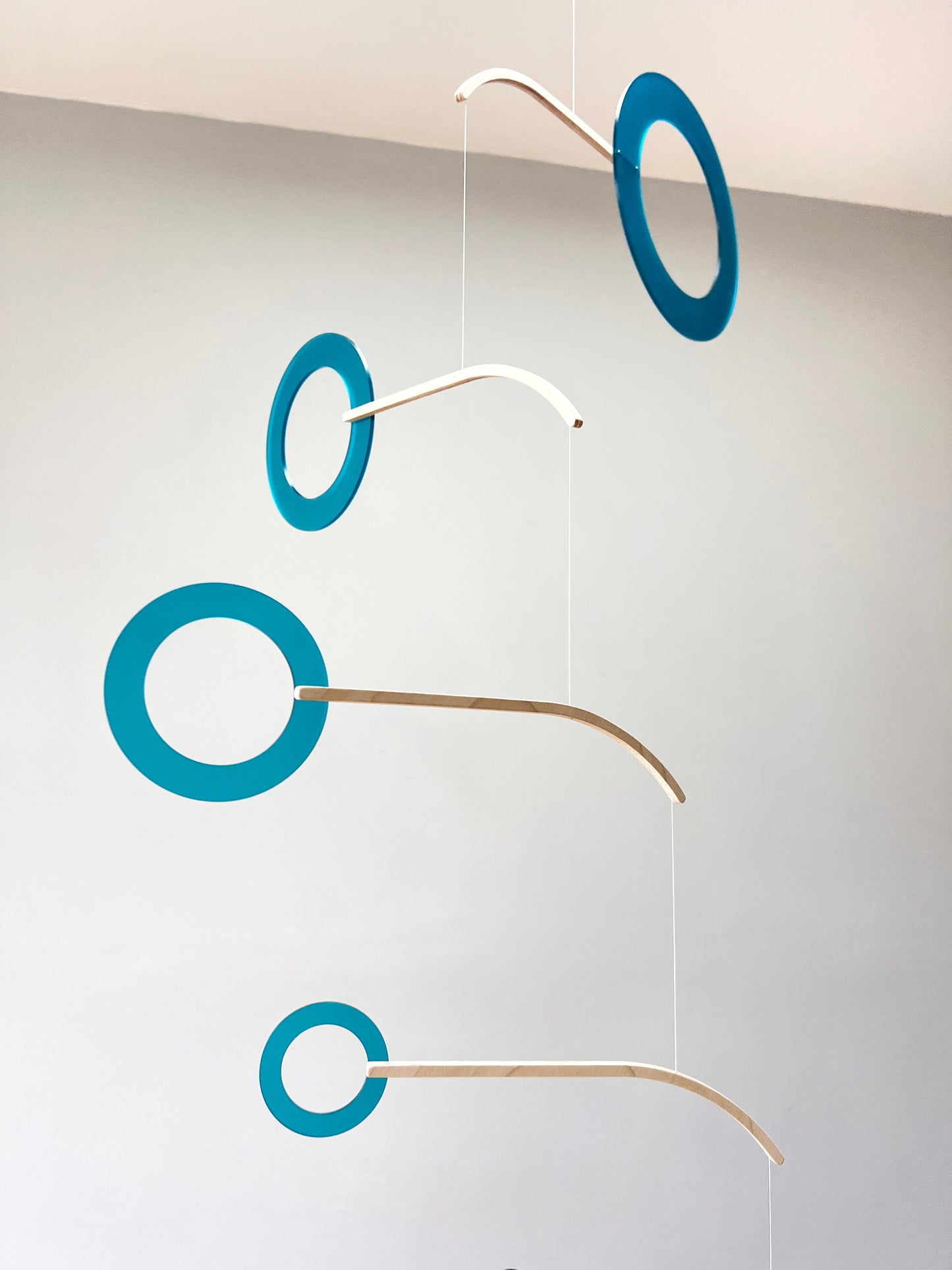 Teal Kinetic Hanging Mobile Sculpture, Minimalistic Circles Adult Mobile Home Decor - Halo Halo Handcrafted By The Illuminist

Introducing Halo Halo Mobile - A stunning piece of kinetic art that will bring movement and interest to any room. Handcrafted from responsibly sourced engineered birch, this unique mobile features six halo rings of increasing width and size in frosted Orange acrylic. Similar to my original Halo mobile but on a verticle plane. 
