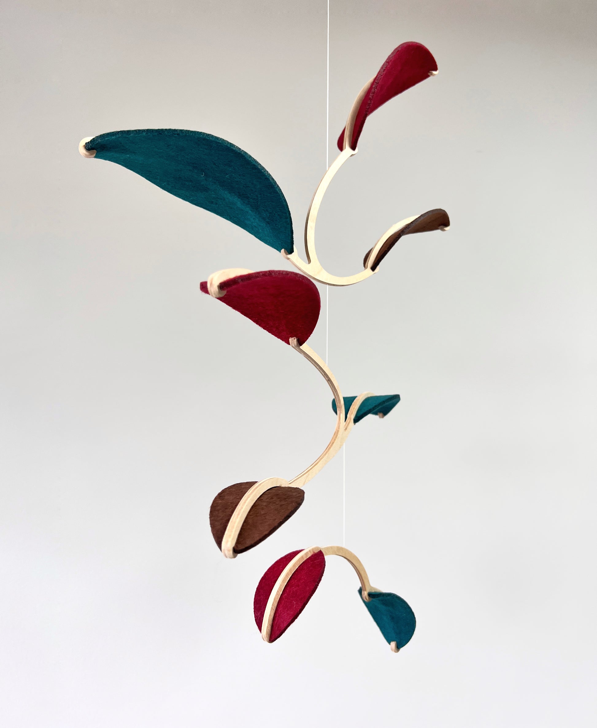 Felt & Wood Leaf Mobile, Adult or Baby Mobile Gift Idea, Plant inspired Sculpture, Kinetic Art Mobile. Maroon, Teal and Brown. 

This vibrant felt leaf mobile is a charming addition to your home decor, offering a lightweight and artistic touch. Handmade with colorful felt leaf shapes, it features independently rotating wooden stems crafted from birch wood, arranged in a customizable color order that can be adjusted anytime.