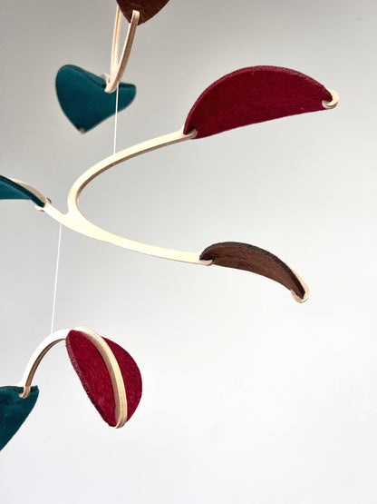 Felt & Wood Leaf Mobile, Adult or Baby Mobile Gift Idea, Plant inspired Sculpture, Kinetic Art Mobile. Maroon, Teal and Brown. 

This vibrant felt leaf mobile is a charming addition to your home decor, offering a lightweight and artistic touch. Handmade with colorful felt leaf shapes, it features independently rotating wooden stems crafted from birch wood, arranged in a customizable color order that can be adjusted anytime.