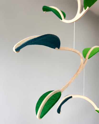 Felt Leaf Mobile 

   Elevate your space with this versatile Midcentury Modern Mobile, designed for both nurseries and adult living areas. Crafted from natural wood with deep teal and green shades of soft felt, this handmade nursery mobile embodies a minimalist and Scandinavian aesthetic. Its unique geometric design creates a stunning hanging sculpture that fits seamlessly into nursery decor and neutral relaxing spaces. 